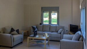 Een woonkamer met een bank, twee fauteuils, een salontafel en een televisie.