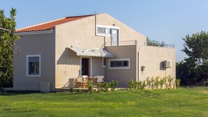 Een woonhuis met twee verdiepingen, een rood pannendak, een balkon en een klein terras met tuinmeubilair.