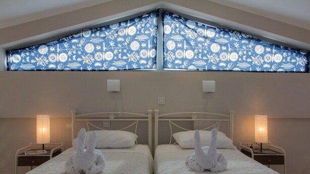 Een kamer met twee eenpersoonsbedden, elk met een witte handdoek en een nachtkastje met een lamp.