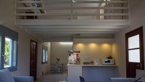 Een ruime woonkamer met een hoge plafond, een keuken met een magnetron, en een eethoek met stoelen.