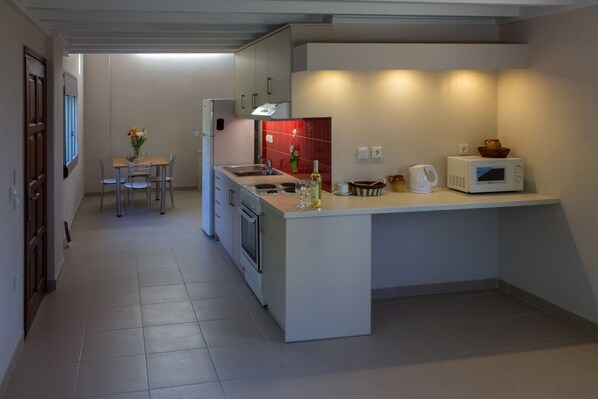 A compact kitchen with a central island, a dining area with a table and chairs, and a refrigerator.