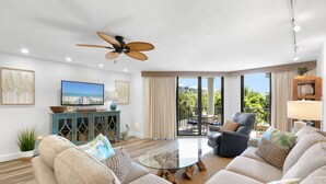 A spacious living room with a glass coffee table, comfortable sofas, a ceiling fan, and a large window offering a view of the outdoors. - ATLANTIC BREEZE ~ 2B/2BA Renovated Retreat w/ Pool, Fitness Area & Beach! (Key West)