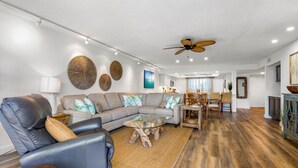 A modern living room with a sectional sofa, a glass coffee table, and a wooden floor. - ATLANTIC BREEZE ~ 2B/2BA Renovated Retreat w/ Pool, Fitness Area & Beach! (Key West)
