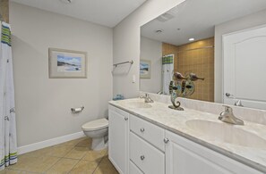 A bathroom with a toilet, two sinks, a large mirror, and a shower area. - Gorgeous Bayfront condo by Seaside Vacations & Sales (Ocean City)