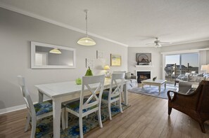A spacious living room with a fireplace, a dining area with a white table and chairs, and a balcony with a view. - Gorgeous Bayfront condo by Seaside Vacations & Sales (Ocean City)