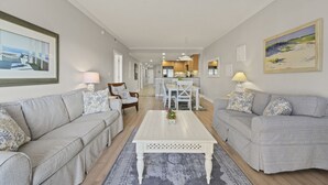 Un salon moderne avec des canapés gris, une table basse blanche et un coin repas comprenant une table et des chaises blanches.