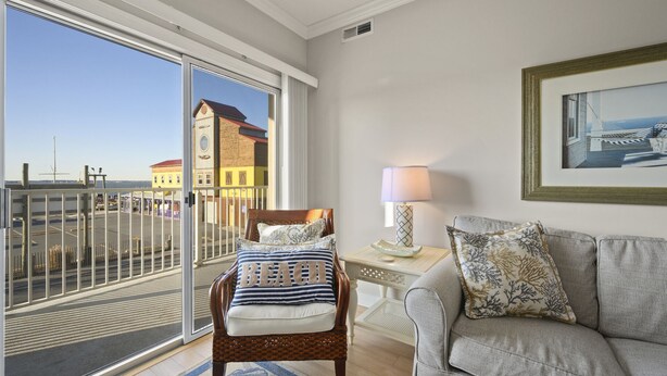 Une chambre avec un balcon, un lit agrémenté d’un coussin orné du mot « PLAGE », un canapé gris, une lampe et un tableau encadré au mur.