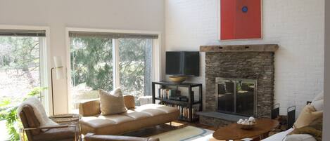 A spacious living room with a stone fireplace, large windows, and a modern TV stand.
