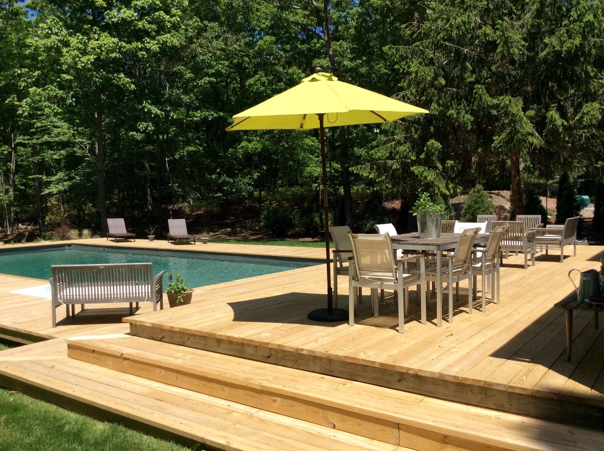 A wooden deck with a pool, outdoor furniture, and a yellow umbrella.