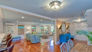 A spacious living room with hardwood flooring, a dining area with a wooden table and chairs, and a blue cabinet. - SOUTHERNMOST BELLE~ Heated Pool, Gourmet Kitchen & Elegant Large Bedrooms! (Key West)