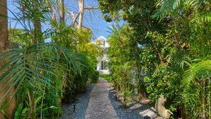 A pathway leading to a white building surrounded by lush greenery. - SOUTHERNMOST BELLE~ Heated Pool, Gourmet Kitchen & Elegant Large Bedrooms! (Key West)