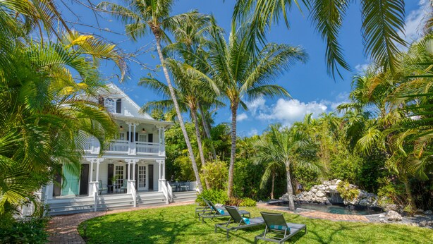 A two-story house with a porch, surrounded by palm trees and a small pond. - SOUTHERNMOST BELLE~ Heated Pool, Gourmet Kitchen & Elegant Large Bedrooms! (Key West)