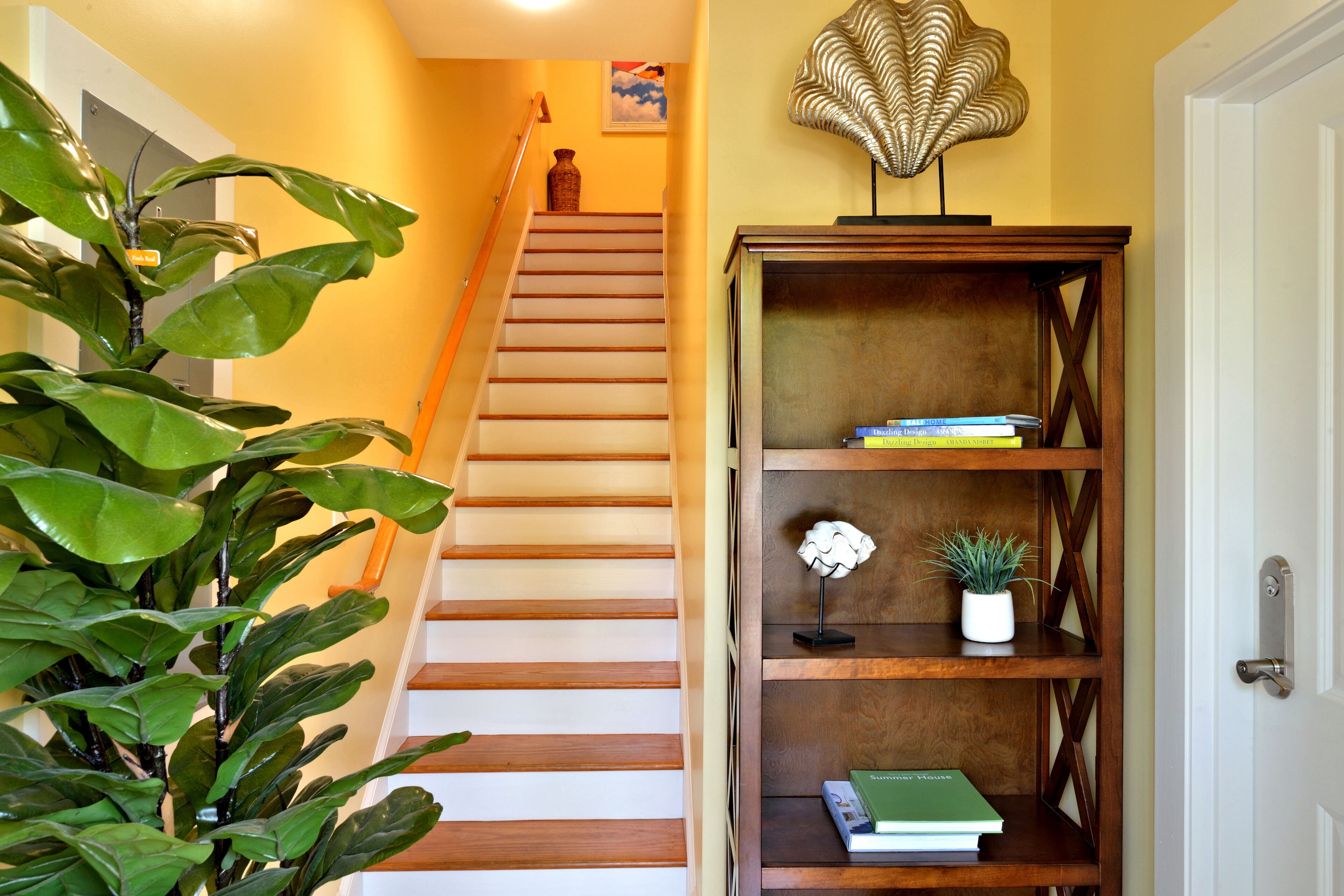 A staircase with wooden steps leading to a landing, a bookshelf with books and decorative items, and a potted plant on the landing.