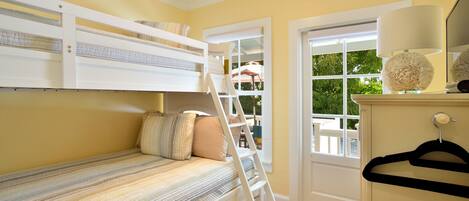 A room with a bunk bed, a ladder, a door, and a window with a view of greenery outside.