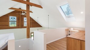 Ein Schlafzimmer im Dachgeschoss mit hohen Decken, Holzbalken, Dachfenster und großen Fenstern.