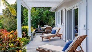 A covered outdoor patio with wooden lounge chairs and a table, surrounded by lush tropical plants. - ONE PALM HILL - Luxury Villa with Private Pool, Walk to Twin Coves Beach (Governors Harbour)