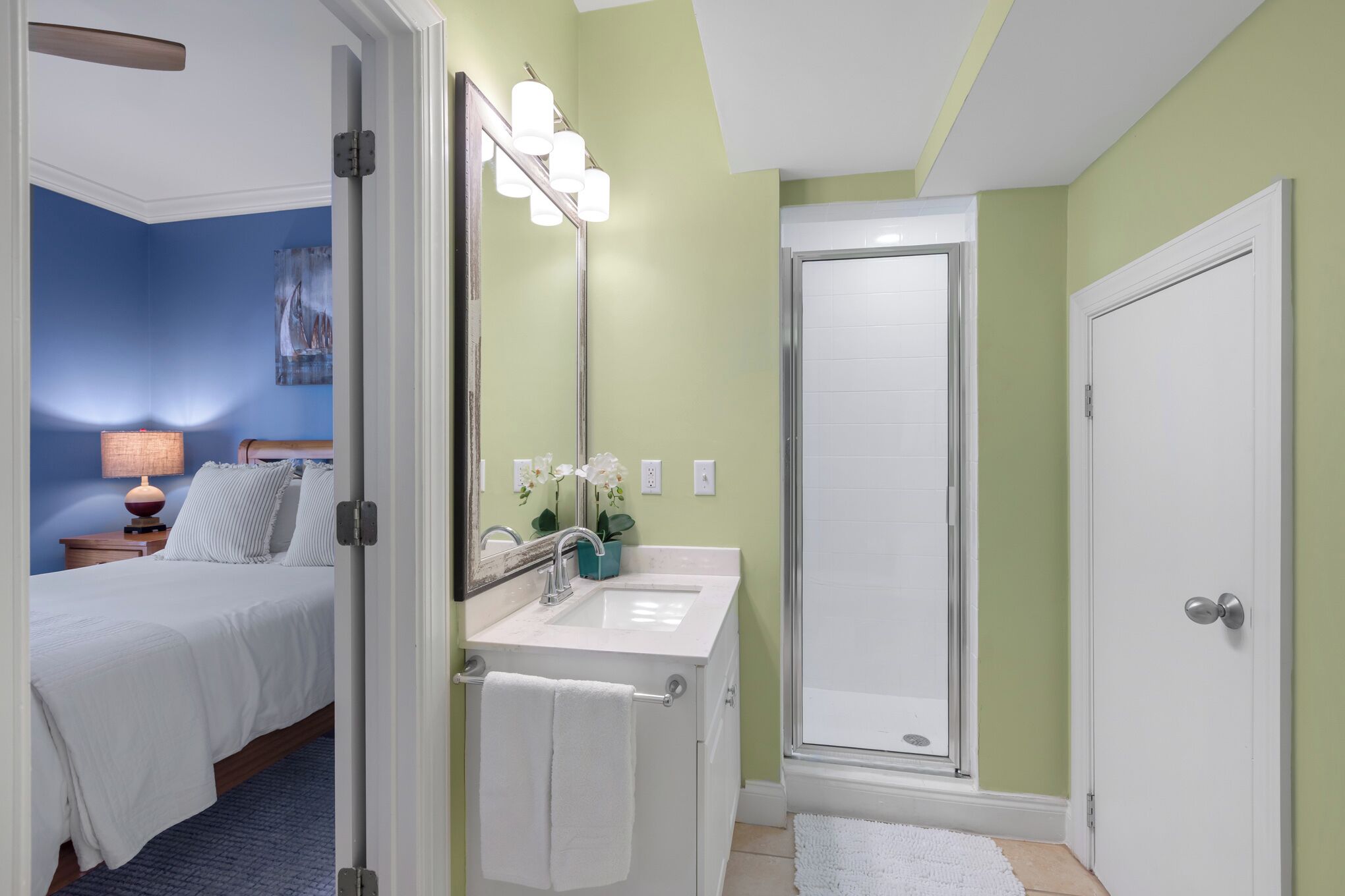 Een slaapkamer met een bed, een badkamer met een wastafel en spiegel, en een douche.