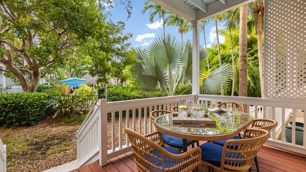 A covered outdoor patio with a round glass table, wicker chairs, and a white railing. - CASA DE VINO ~ Amazing Price for  Charming Townhouse with Pool & Tiki! (Key West)