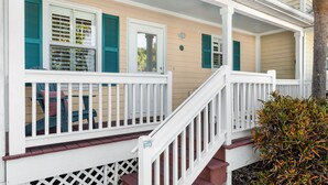 A porch with white railings and a red staircase leading up to a beige house with teal shutters. - CASA DE VINO ~ Amazing Price for  Charming Townhouse with Pool & Tiki! (Key West)