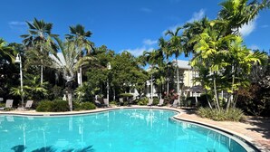 A clear blue swimming pool surrounded by palm trees and lounge chairs, with a clear sky above. - CASA DE VINO ~ Amazing Price for  Charming Townhouse with Pool & Tiki! (Key West)