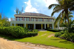 A large, two-story building with a balcony, surrounded by well-maintained gardens and palm trees. - Private Beachfront Home w/Pool, Solar, Banks Rd, Walk to Restaurants (Governors Harbour)