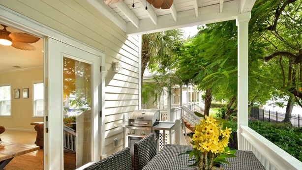 Un patio cubierto con una parrilla, mobiliario exterior y vistas al jardín trasero.