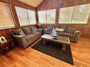 A cozy living room with wooden walls, two sofas, a coffee table, and a sailboat model. - Cozy Home, Lots of Light, Three Blocks from Beach (NARRAGANSETT)