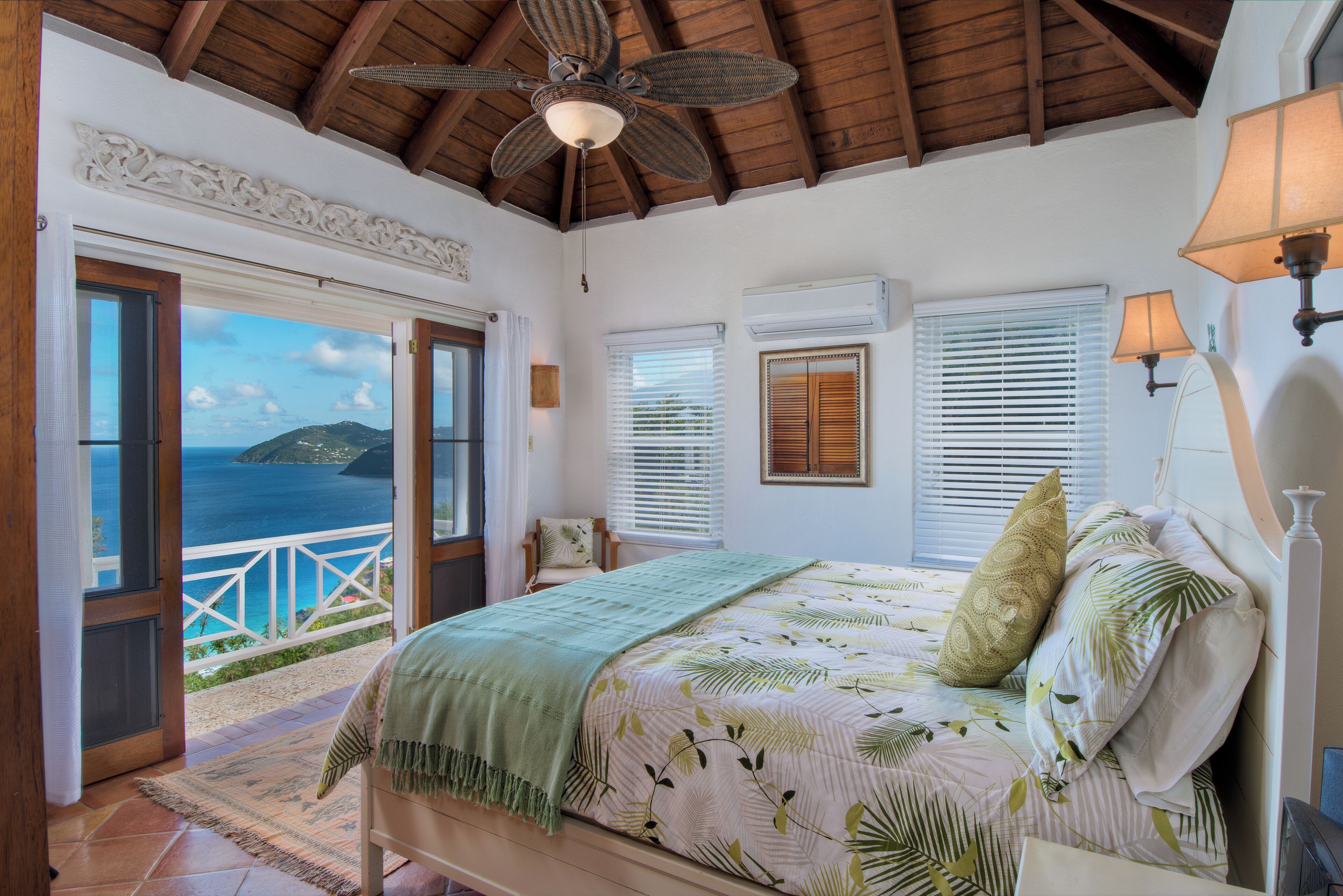 Een slaapkamer met een bed, uitzicht op zee en een balkon.