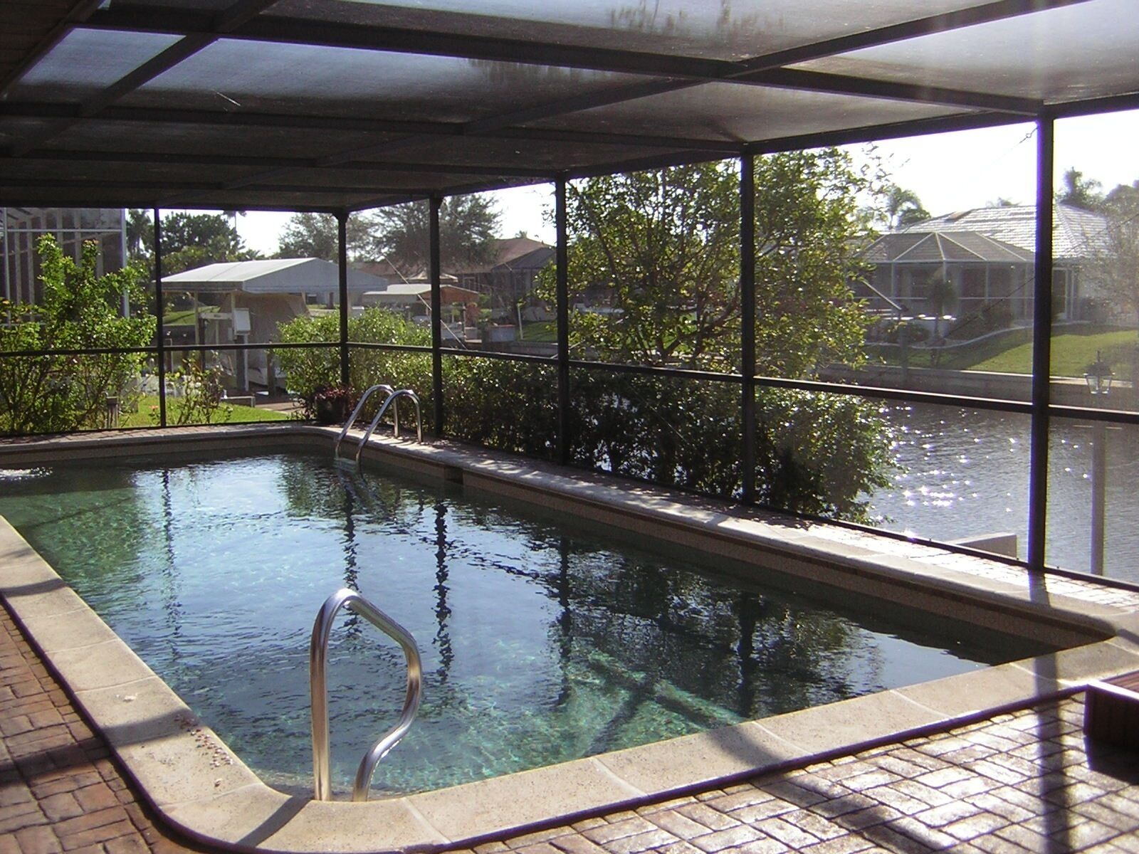 An indoor swimming pool with clear water, a metal ladder, and a view of houses through large windows.