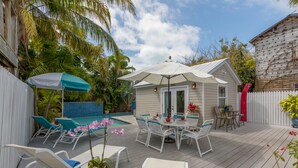 A deck with outdoor furniture, a pool, and a small building with a red door. - LADY ADMIRAL ~Sweet cottage & guest house with private heated pool off Duval! (Key West)