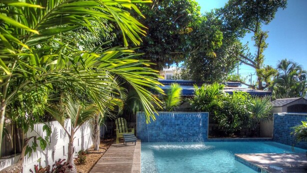 A swimming pool with a wooden deck and a blue tiled wall. - LADY ADMIRAL ~Sweet cottage & guest house with private heated pool off Duval! (Key West)
