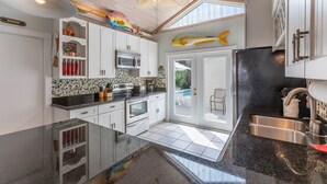 A kitchen with white cabinets, a black countertop, and a ceiling fan. - LADY ADMIRAL ~Sweet cottage & guest house with private heated pool off Duval! (Key West)