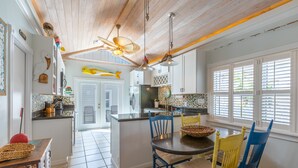 A kitchen with white cabinets, a wooden ceiling, and a dining area with blue and yellow chairs. - LADY ADMIRAL ~Sweet cottage & guest house with private heated pool off Duval! (Key West)