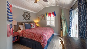 A bedroom with a wooden ceiling, a bed with a red and blue bedspread, a ship's wheel decoration, and a flag on the wall. - LADY ADMIRAL ~Sweet cottage & guest house with private heated pool off Duval! (Key West)