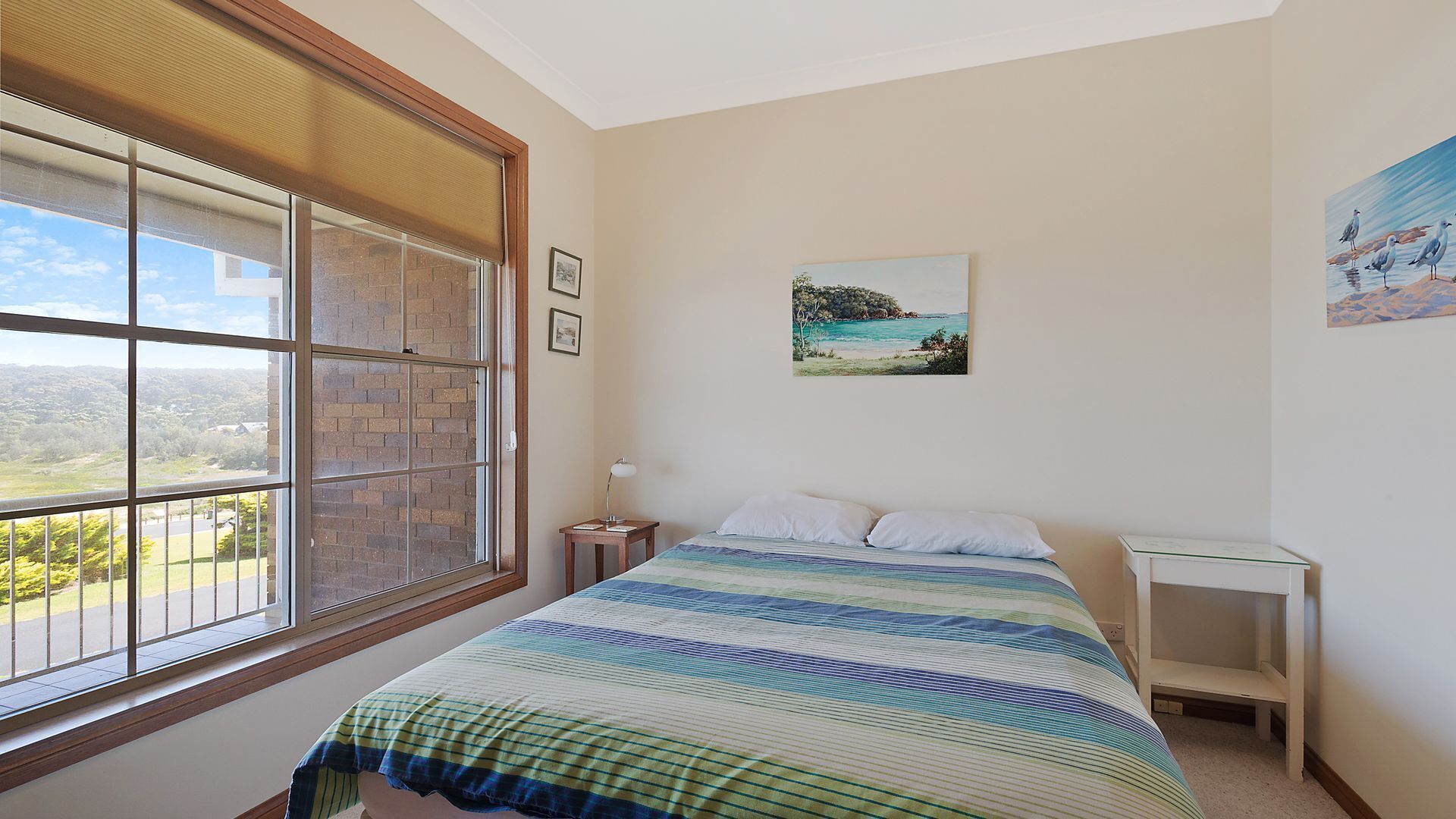 Une chambre avec une grande fenêtre, un lit recouvert d’une courtepointe à rayures, une table de chevet et une commode.