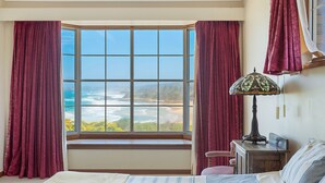 A bedroom with a bay window overlooking a beach, a lamp, and a chair. - 120 Ocean Parade Dalmeny (Dalmeny)