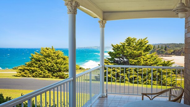 A balcony with a view of the ocean and beach, a chair, and a railing. - 120 Ocean Parade Dalmeny (Dalmeny)
