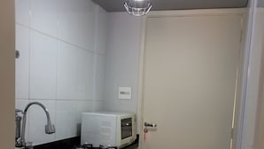 A kitchen with a microwave, sink, and cabinets. - Cozy Kitnet At The Beach (Ponta da Praia)