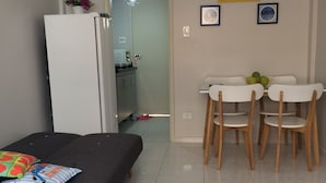 A compact living space with a sofa, a dining table with chairs, a refrigerator, and a kitchen area visible through an open door. - Cozy Kitnet At The Beach (Ponta da Praia)