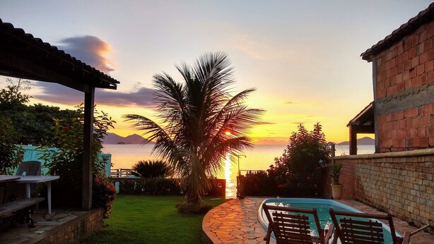 A patio with a pool, a palm tree, and a sunset view. - House in front of the sea with a beautiful sunrise, deck for good fishing With WI- (Mangaratiba)