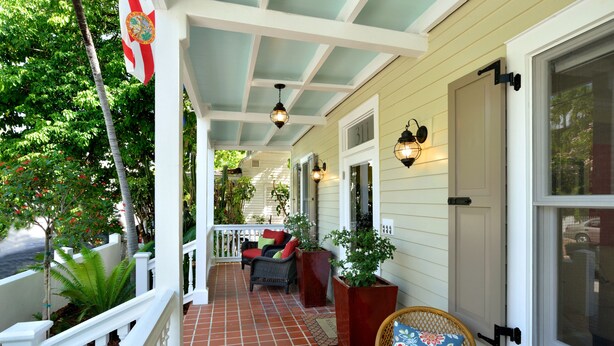 A covered porch with a white railing, a wicker chair, a table, and potted plants. - STARS ~ 4 bedroom, 2 Bath Condo, Shared Heated Pool, Downtown Location! (Key West)