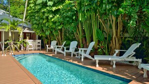 A rectangular swimming pool with clear blue water, surrounded by white lounge chairs and a wooden deck. - STARS ~ 4 bedroom, 2 Bath Condo, Shared Heated Pool, Downtown Location! (Key West)