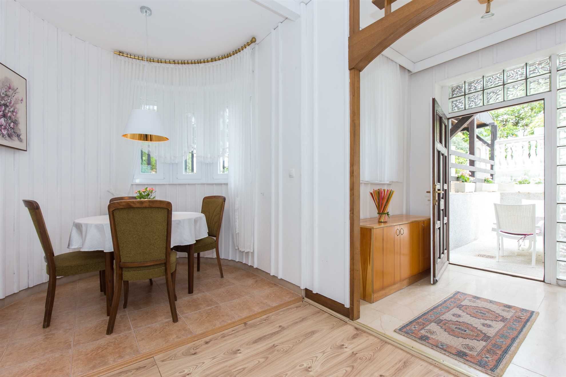 A dining area with a table and chairs, a wooden cabinet, and a view of the outdoors through a glass door.