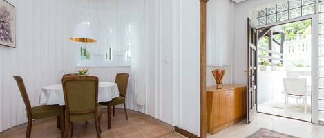 A dining area with a table and chairs, a wooden cabinet, and a view of the outdoors through a glass door.