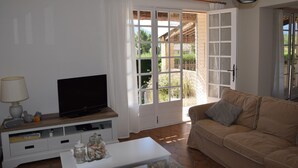 A living room with a television on a wooden stand, a white coffee table, a beige sofa, and a large sliding glass door leading to an outdoor area. - Superb holiday house in the natural beauty of the Gorges de Verdon (Castellane)