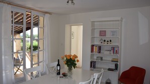 A dining area with a table set for two, a bookshelf, and a view through a window. - Superb holiday house in the natural beauty of the Gorges de Verdon (Castellane)