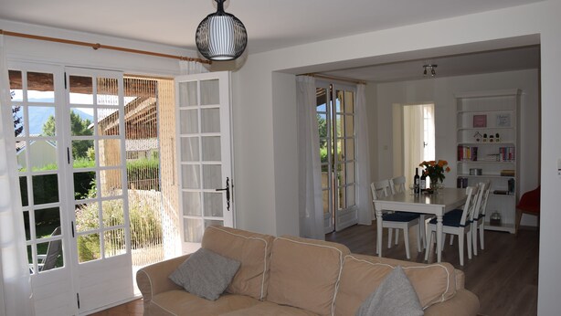 A spacious living area with a beige sofa, a dining table with chairs, and a kitchen area in the background. - Superb holiday house in the natural beauty of the Gorges de Verdon (Castellane)