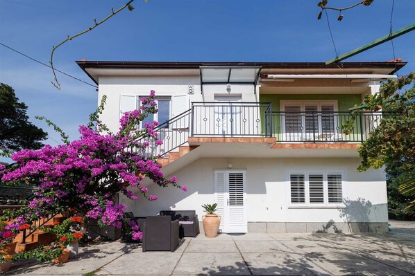 A two-story building with a balcony, a potted plant, and a clear sky.