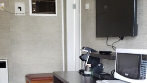 A compact kitchen with a microwave, refrigerator, and a flat-screen TV mounted on the wall.