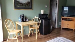A compact living space with a dining table, two chairs, a refrigerator, a microwave, a television, and a small cabinet.